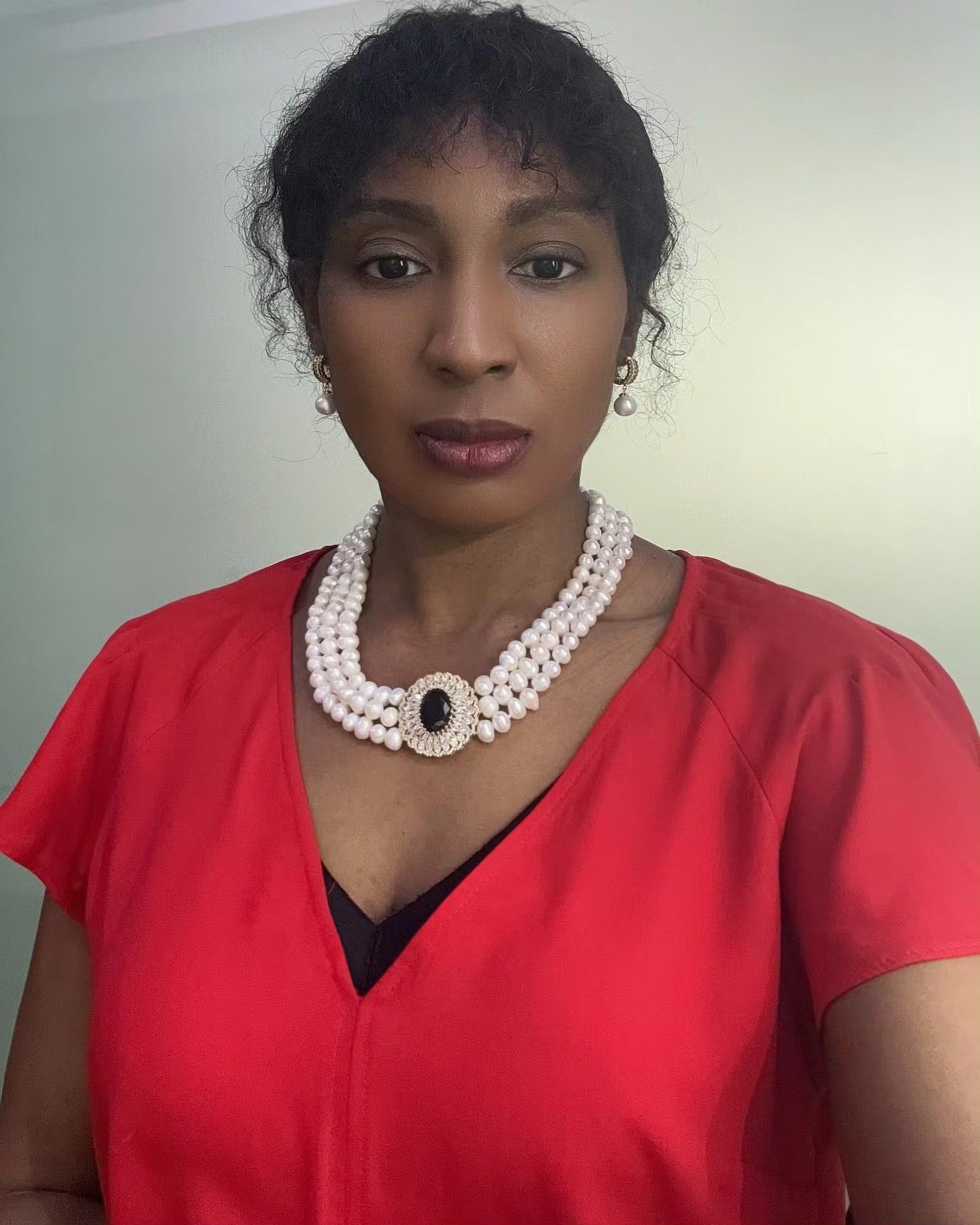 Elegant woman in red dress wearing Murun Pearls triple-strand freshwater pearl necklace with black gemstone centerpiece and matching drop pearl earrings.