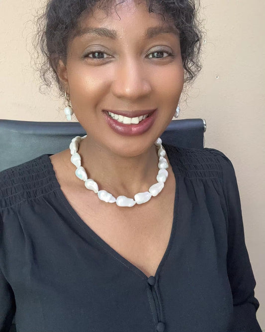 Woman in black blouse smiling while wearing white baroque freshwater pearl necklace and matching pearl drop earrings from Murun Pearls.