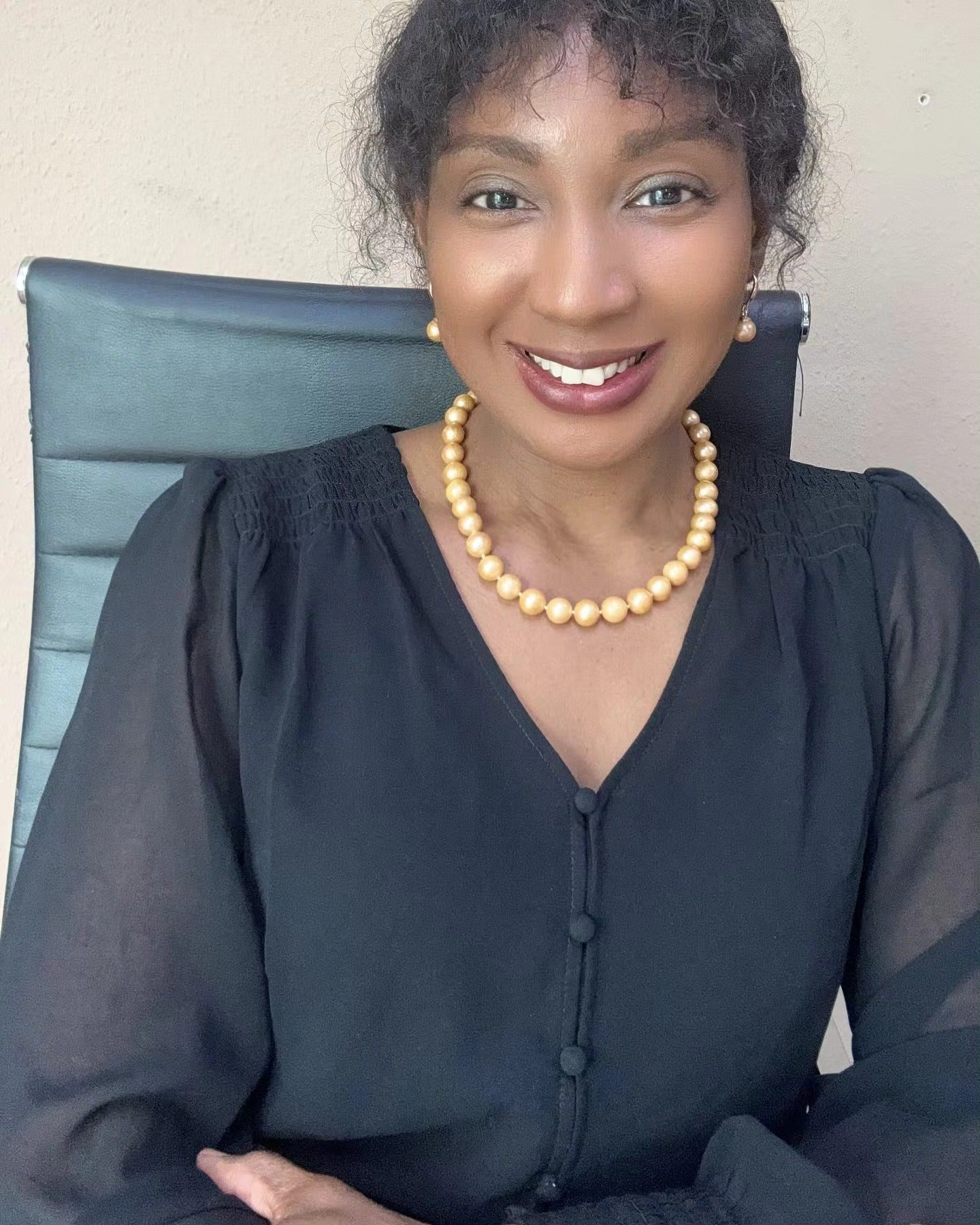 Elegant woman in black blouse smiling while wearing round golden South Sea pearl necklace and matching pearl drop earrings from Murun Pearls.