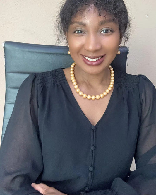 Elegant woman in black blouse smiling while wearing round golden South Sea pearl necklace and matching pearl drop earrings from Murun Pearls.