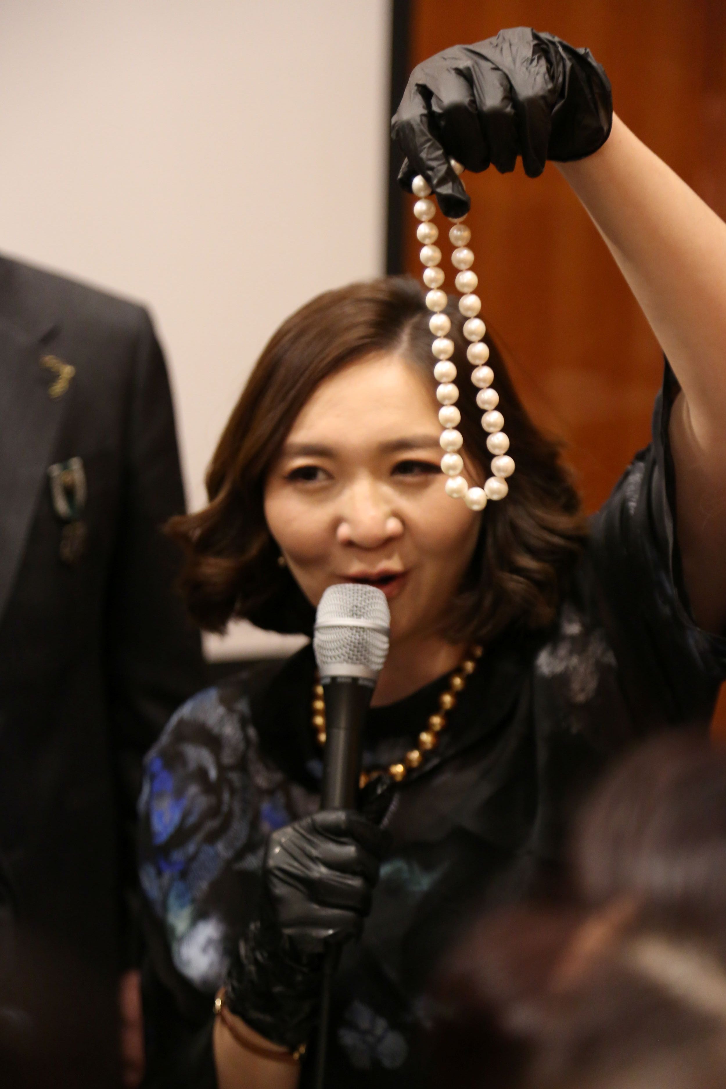 Presenter sharing pearl knowledge with a strand of pearls in hand at a Murun Pearls event